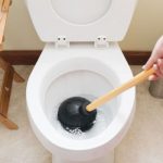 Clean white toilet with a plunger and wooden handle, highlighting plumbing maintenance in a tidy household setting.