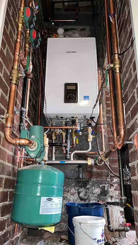 Tankless water heater installation with copper piping and green expansion tank in a residential setting, showcasing plumbing work by Jeffrey Burke Plumbing.