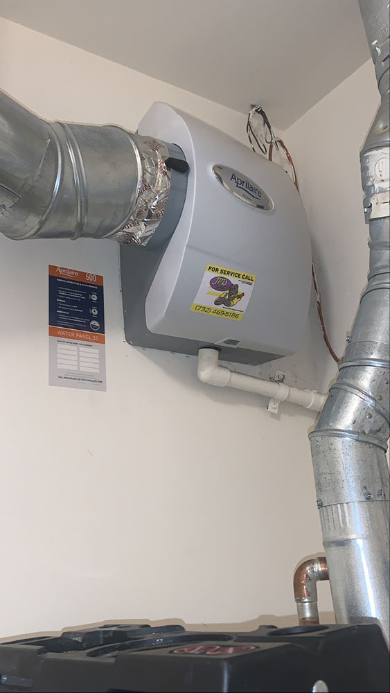 Whole home humidifier installation featuring Aprilaire unit with service call information, pipes, and ventilation, highlighting plumbing and HVAC expertise by Jeffrey Burke Plumbing, Heating & Cooling.