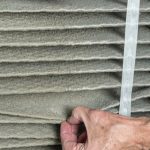 Hand interacting with a dirty, pleated air filter, emphasizing plumbing and HVAC maintenance needs for homeowners.