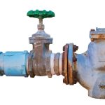 Water valve with green handle and pipeline, showcasing metallic and rusty textures for plumbing maintenance.