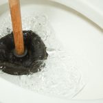 Toilet bowl scene with a plunger and water splashing, highlighting plumbing maintenance by Jeffrey Burke Plumbing.