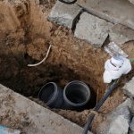 Trenchless pipe repair site showing exposed underground pipes in a dug-out area, emphasizing modern plumbing solutions by Jeffrey Burke Plumbing.